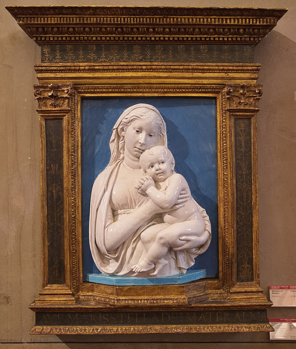 A glazed terracotta relief by Luca della Robbia showing a mother and child, with white figures on a blue background