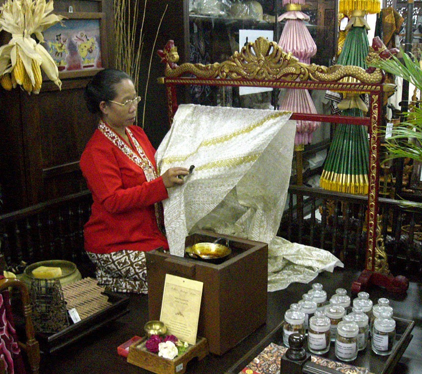 A woman in Indonesia applying liquid wax to fabric using a canting tool to create batik patterns