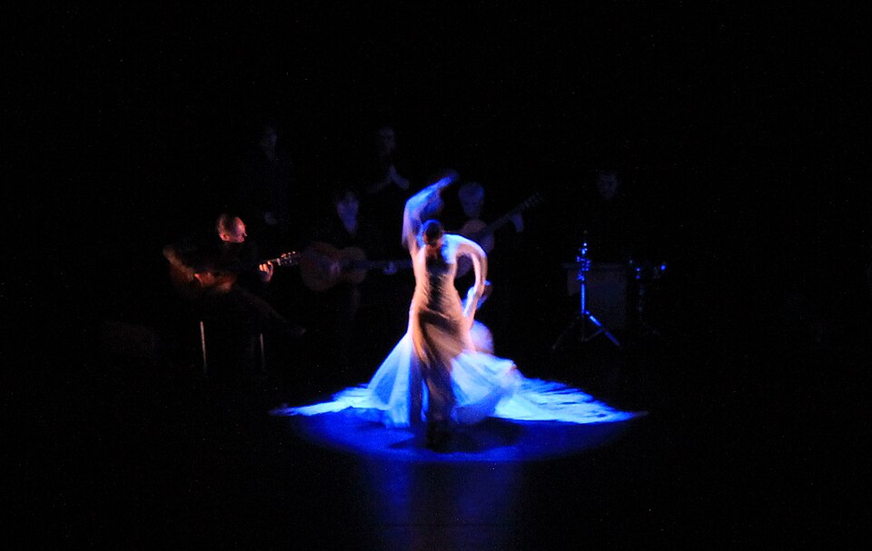 A flamenco dancer performing on stage with a guitarist in the background