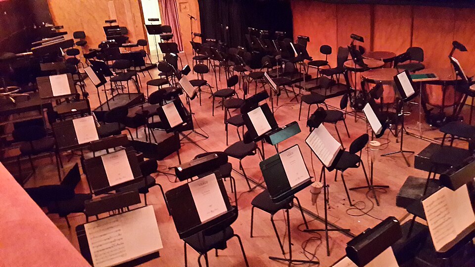 An orchestra pit in a theater with music stands and chairs set up for musicians