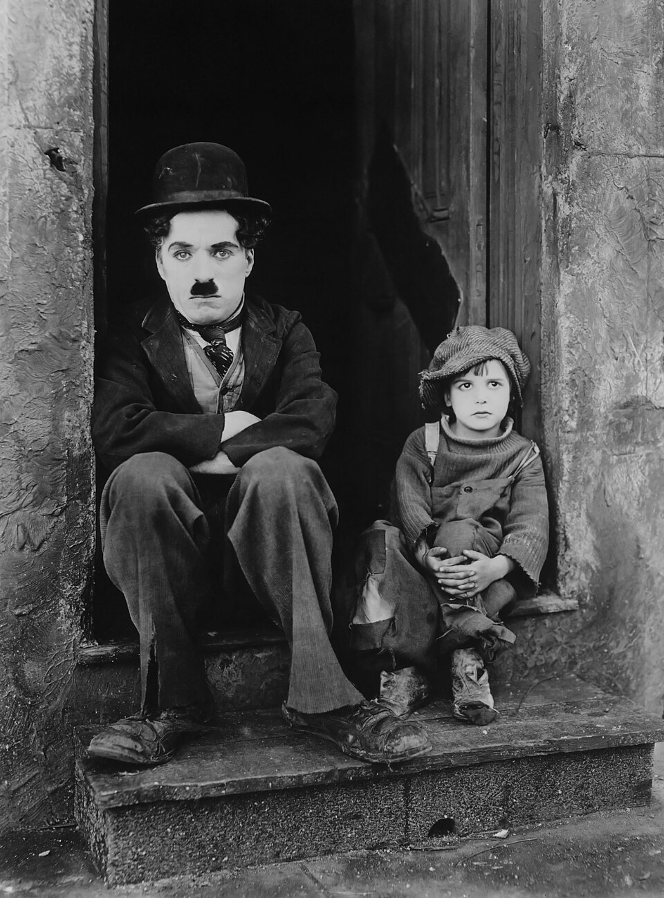Charlie Chaplin and Jackie Coogan sitting on a doorstep in the 1921 silent film The Kid