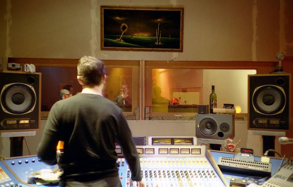 An audio engineer works at a large mixing console in a professional recording studio