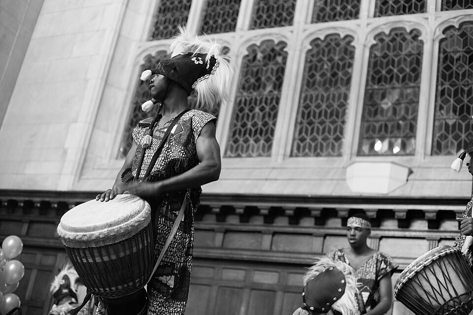 A young drummer playing a djembe drum in traditional West African clothing