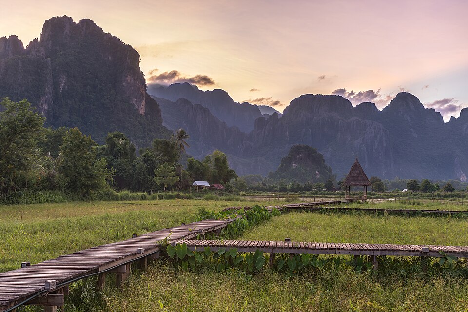 A beautiful landscape photograph of mountains at sunset with a wooden walkway leading to a hut