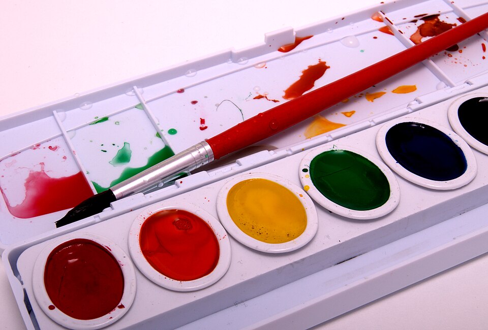 A set of watercolor paints with a red paintbrush
