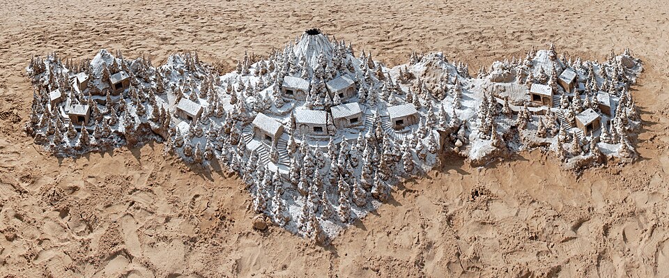 A detailed sand sculpture of a tiny village on a beach