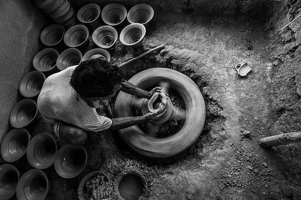 A potter shaping clay on a spinning pottery wheel with finished pots nearby