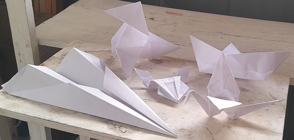 Traditional origami figures including a bird, boat, airplane, jumping frog, and crane made from white paper