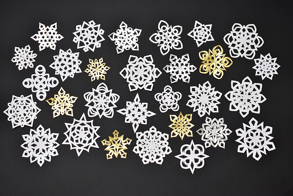 Many beautiful paper snowflakes in white and gold arranged on a dark background