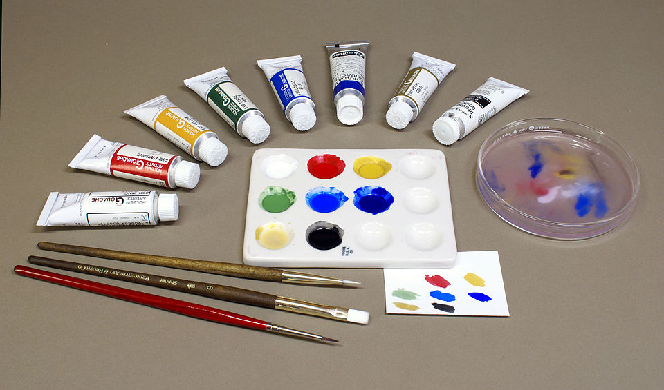 A paint palette with tubes of paint and brushes showing red, blue, yellow, and other colors