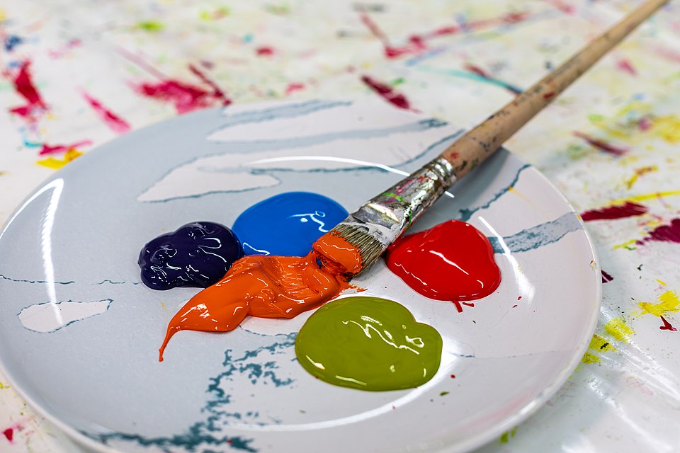 A paint palette with bright blobs of blue, red, orange, green, and purple paint and a brush