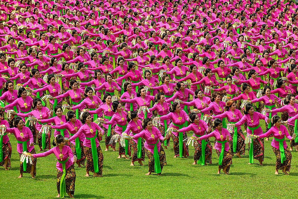Hundreds of dancers in bright pink costumes performing the Pendet folk dance in Indonesia