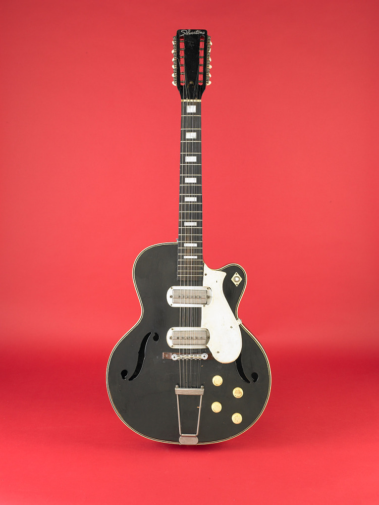 A black Silvertone electric guitar against a bright red background