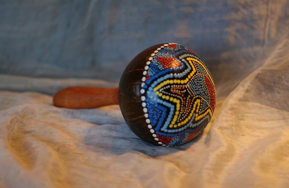 A colorful hand-painted maraca with bright dot patterns in blue, red, and yellow