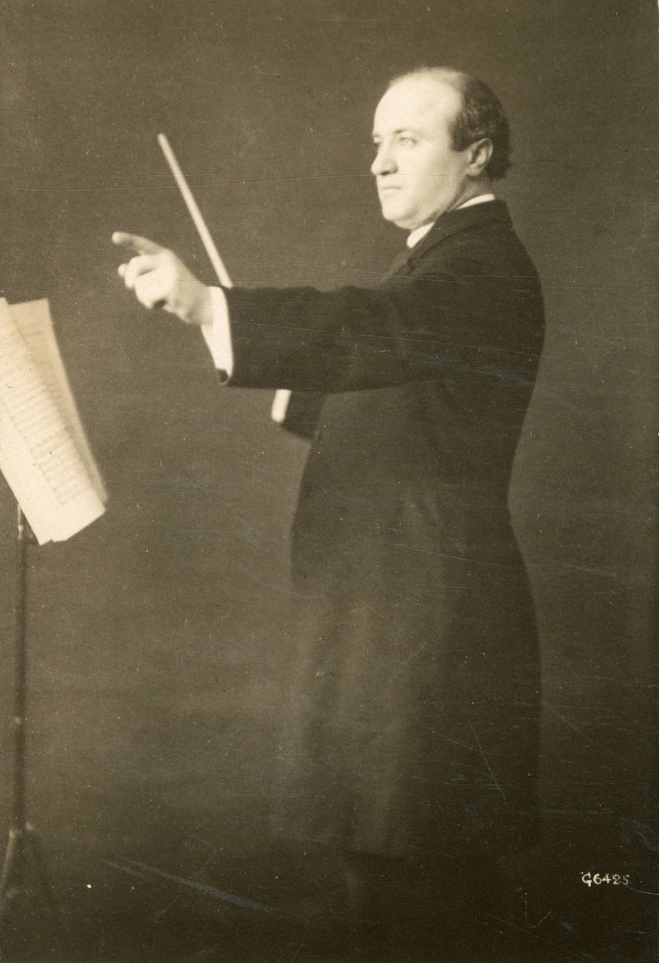 An orchestra conductor holding a baton and standing at a music stand