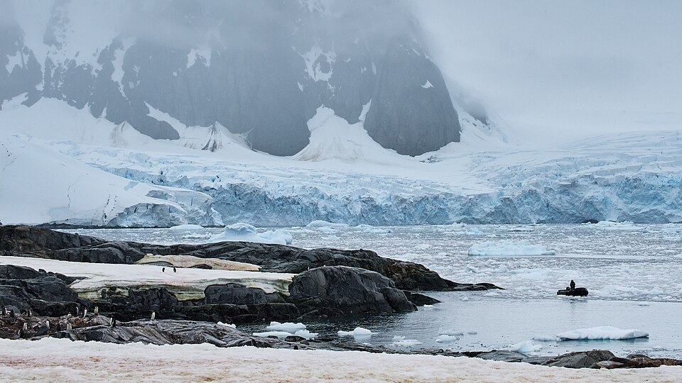 Penguins standing on rocky shores in Antarctica with glaciers and icy mountains in the background