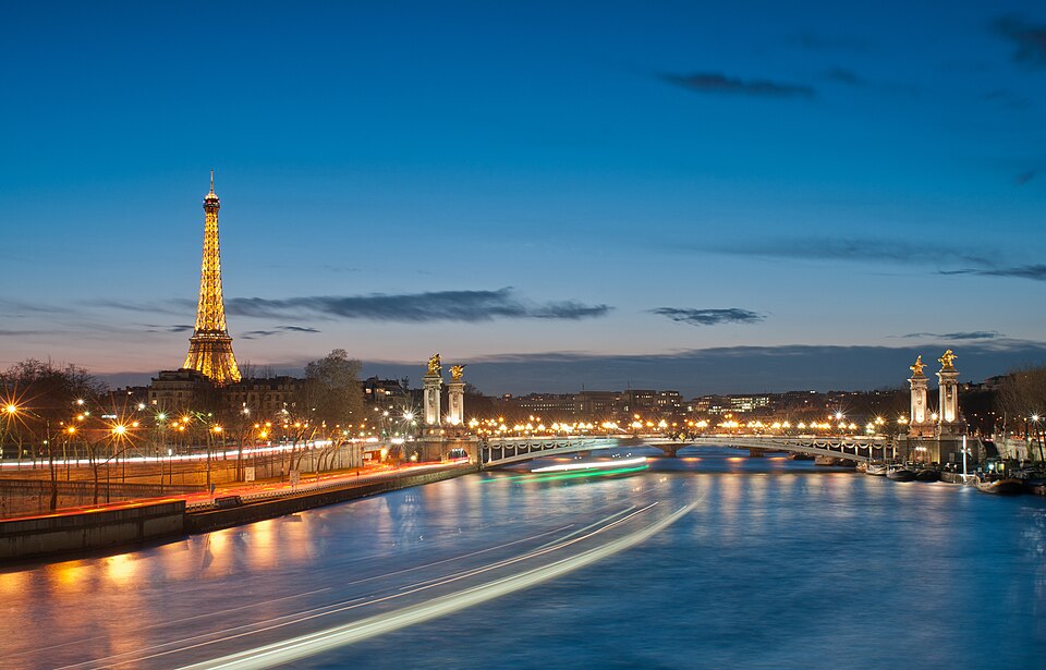 The Eiffel Tower glowing at night along the Seine River in Paris