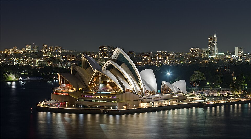 The Sydney Opera House lit up at night on the harbour with city lights behind it