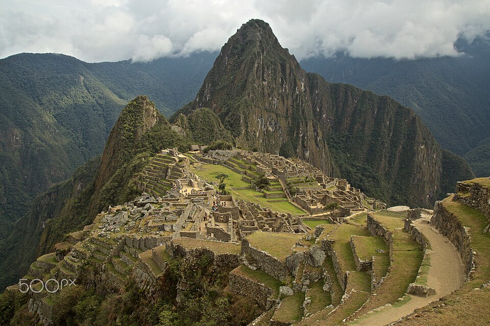 The stone ruins of Machu Picchu with green mountains and clouds behind them