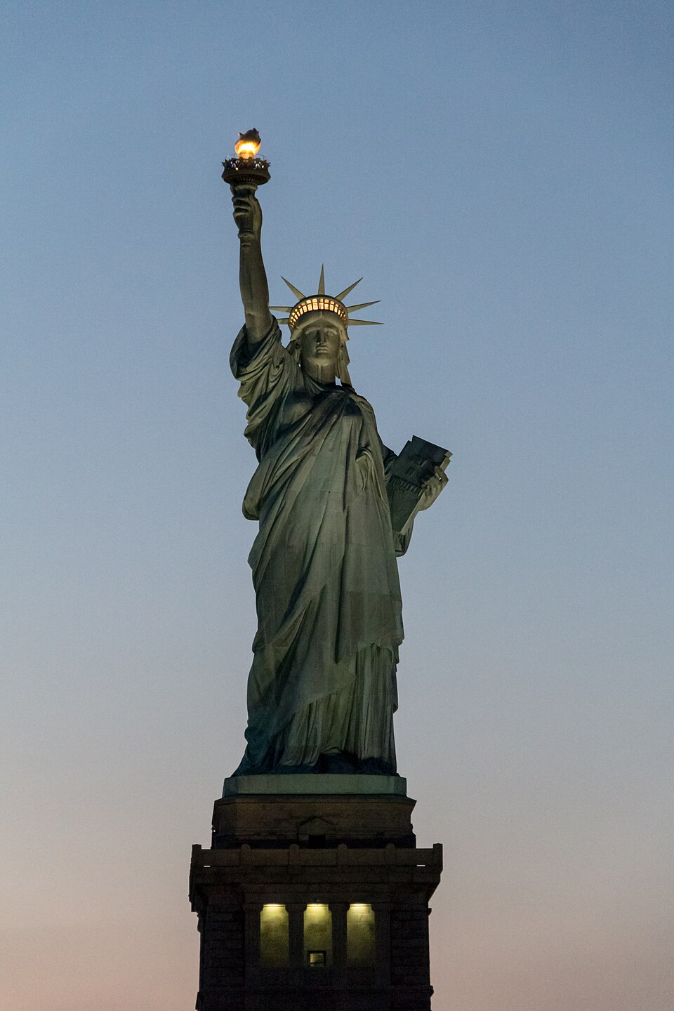 The Statue of Liberty at dusk with her glowing torch and crown