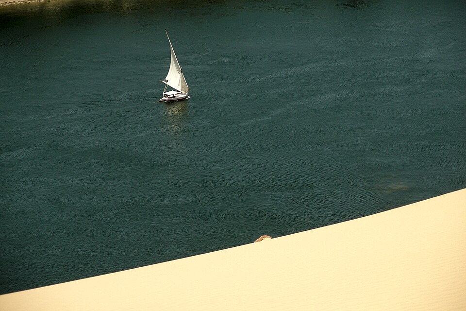 A felucca sailboat gliding along the Nile River in Egypt with sandy desert on the shore