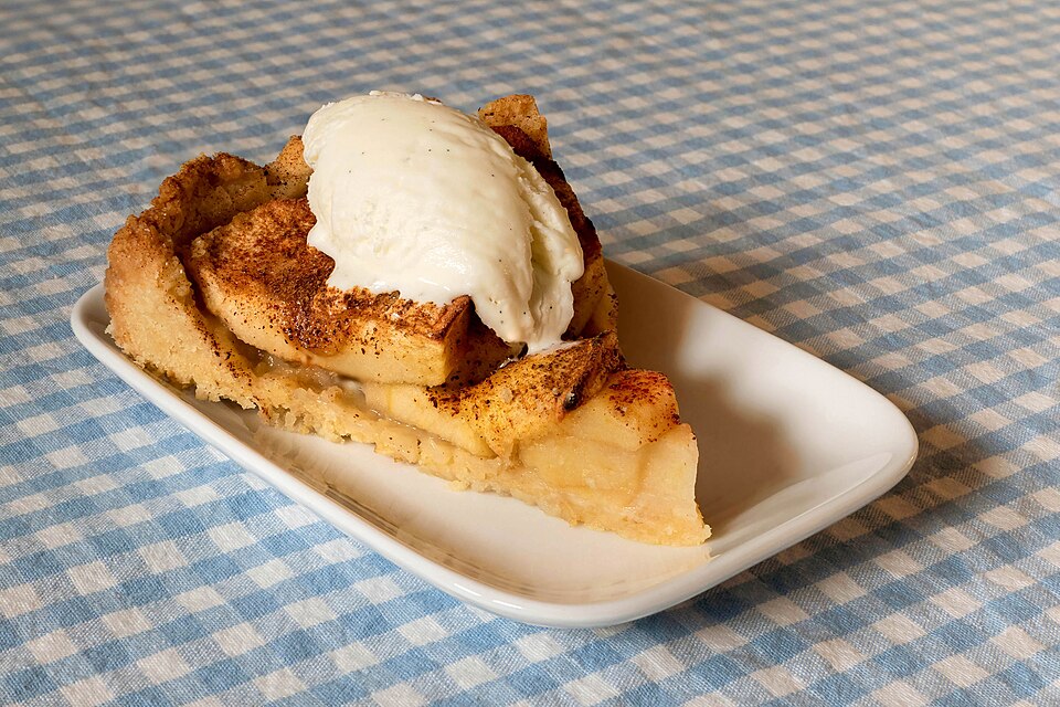 A scoop of vanilla ice cream on top of apple pie