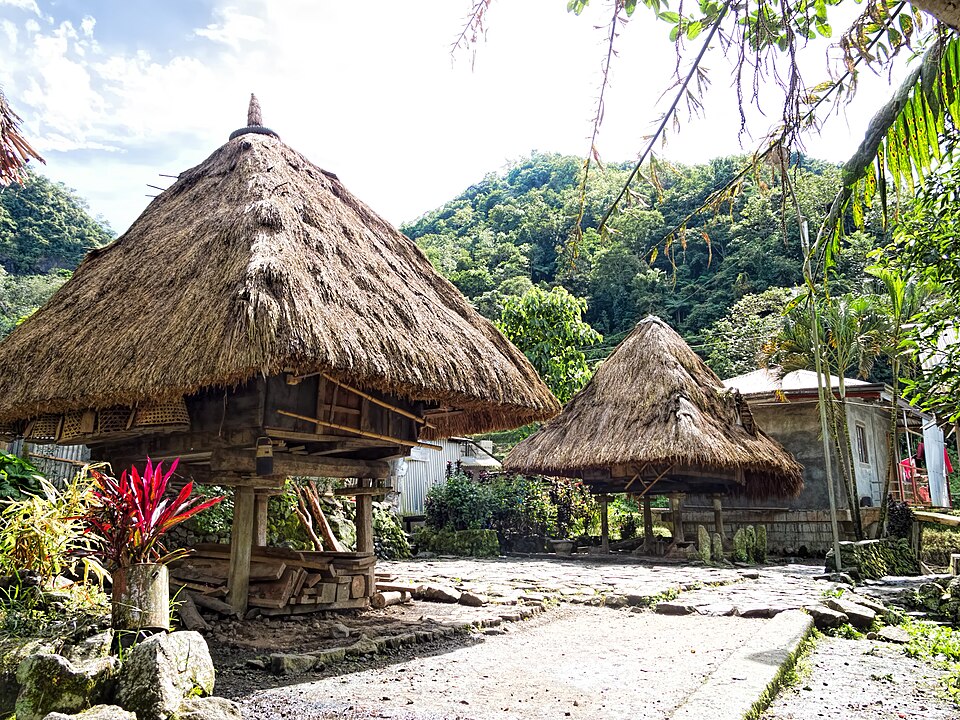 Traditional stilt houses with thatched roofs in a village in the Philippines, surrounded by tropical forest and mountains