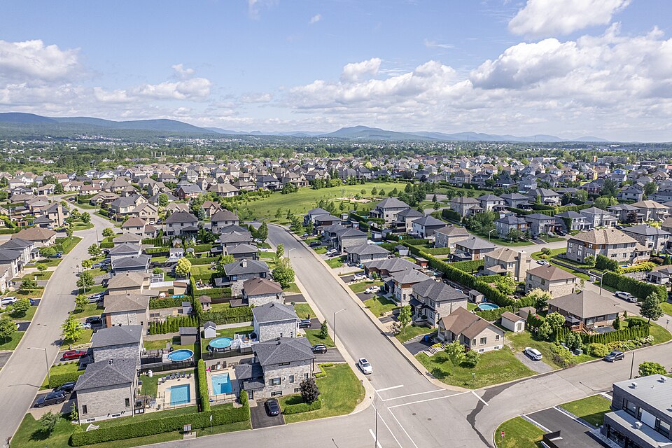 Aerial view of a suburban neighborhood with many single-family houses, green lawns, and winding streets