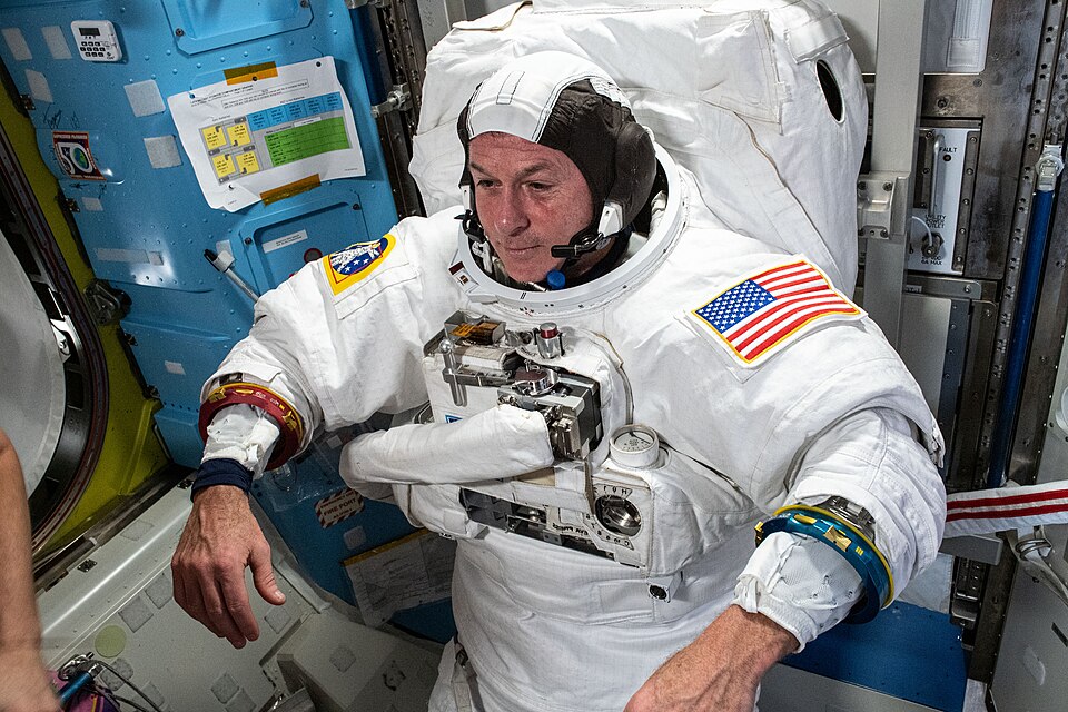 An astronaut trying on a white spacesuit inside the space station before a spacewalk