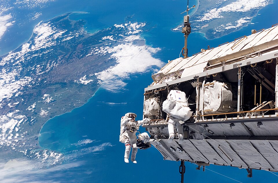 Two astronauts on a spacewalk outside the International Space Station with Earth below